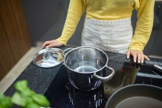 Personne âgée cuisinant dans une cuisine équipée d'une plaque de cuisson
